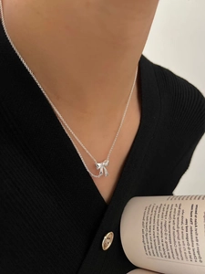 Detail of a double-layered sterling silver necklace with a ribbon bow pendant on a model