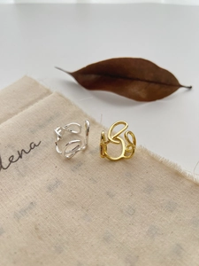 Detailed view of abstract twisted silver and gold open rings on a minimalist fabric background