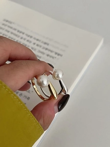 Macro shot of S925 sterling silver pearl rings in gold and silver held by a model