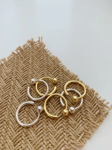 Detailed close-up of polished silver and gold bead open rings on a textured linen fabric