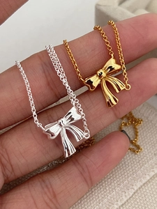 Detailed macro view of polished gold and silver bow ribbon necklaces held in fingers
