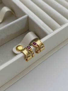 Detail of 925 silver gold earrings with rectangular red cubic zirconia on beige velvet