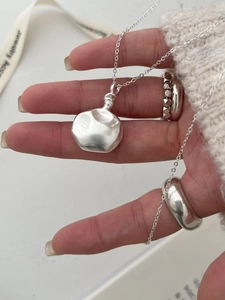 Détail du collier avec pendentif argenté irrégulier et bagues sur un pull blanc