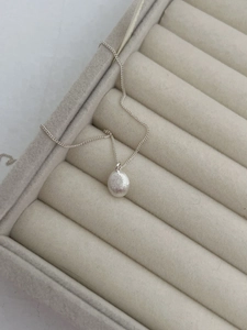Macro detail of S925 sterling silver ball necklace with matte brushed finish on gray velvet