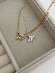 Close-up of gold and silver bow necklaces in a luxury jewelry box with ribbon details