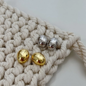 Minimalist bean-shaped metal stud earrings in gold and silver set on woven texture