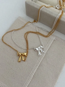 Close-up of gold and silver bow pendant necklaces on textured beige fabric