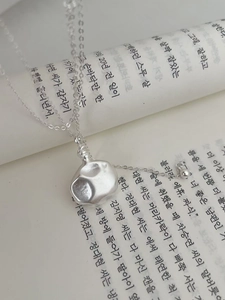 Détail du pendentif en argent S925 martelé avec texture irrégulière sur fond de livre
