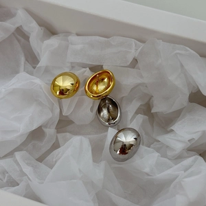 Minimalist polished bean stud earrings in gold and silver finishes on textured background