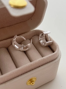 Close-up of polished silver hoop earrings placed in a beige velvet jewelry box