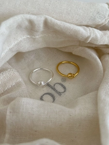 Close-up of gold and silver knot rings on a soft beige drawstring fabric bag