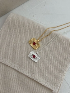 Detail of gold and silver sunburst necklaces with red stones on a textured surface