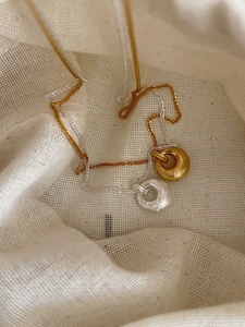 Détail de pendentifs minimalistes en or et argent sur tissu en coton blanc