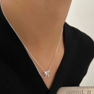 Minimalist sterling silver ribbon bow necklace worn by a model on a black knit top