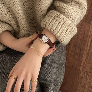 Vintage women's square gold watch with brown leather strap and layered gold rings