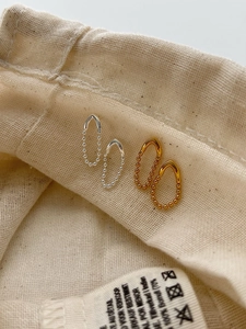 Détail de boucles d'oreilles en chaîne en V argentées et dorées sur un sac en lin
