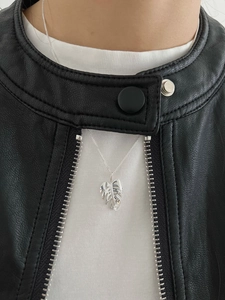 Détail macro du collier feuille de Monstera en argent avec zircon sur fond de veste noire
