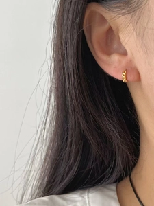 Détail macro de boucles d'oreilles créoles dorées torsadées portées par un mannequin