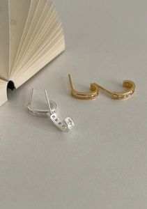 Dettaglio di orecchini a semicerchio a C con zirconi in finiture oro e argento