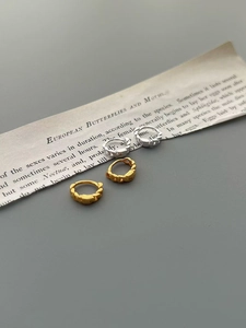 Détail de boucles d'oreilles créoles torsadées argent et or avec zircon sur papier