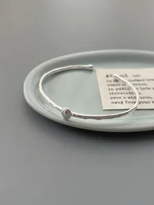 Macro detail of silver open bangle with hammered texture and oval accent in a ceramic tray