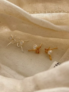 Détail de boucles d'oreilles nœuds en argent 925 et or avec perles blanches sur tissu