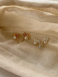 Détail de boucles d'oreilles nœuds dorées et argentées avec perles blanches sur tissu