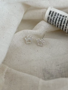 Macro shot of silver hollow cat paw ear threaders with cubic zirconia on white fabric