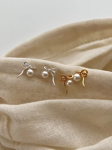 Détail macro de boucles d'oreilles nœuds dorés et argentés avec perles blanches rondes