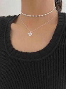 Close-up of layered silver iris pendant necklace and pearl choker on female model neck