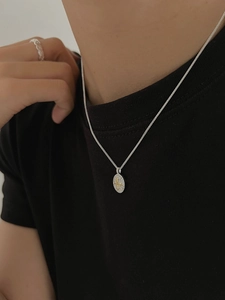 Close-up of silver fleur-de-lis oval necklace with zircon inlay on model wearing black