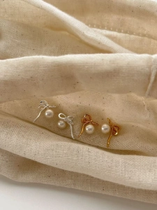 Détail de boucles d'oreilles nœuds argent et or avec perles sur tissu texturé