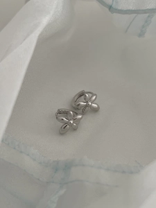 Macro shot of silver metal flower earrings on a textured white fabric background