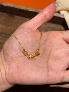 Détail macro d'un collier doré avec trois pendentifs fleurs et gemmes violettes