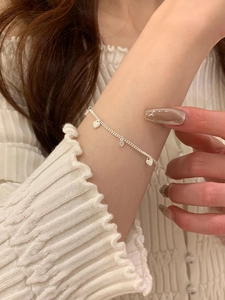 Close-up of S925 sterling silver chain featuring heart and zircon charms on model's wrist