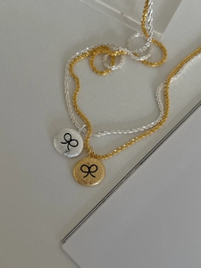 Close-up of brushed metal pendant necklaces with black bow engraving in gold and silver