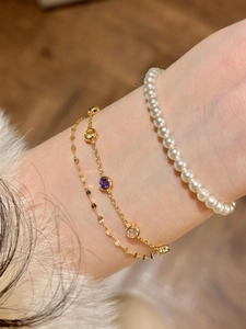 Détail de bracelets dorés superposés avec perles blanches et pierres de zircon colorées