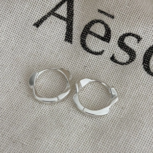 Boucles d'oreilles créoles Mobius en argent 925 avec design torsadé sur un sac en lin