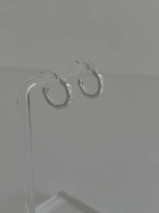 Detail of silver geometric hoop earrings featuring multifaceted edges and white zircons
