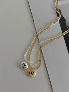 Detail of gold and silver brushed metal round necklaces with black bow engraving