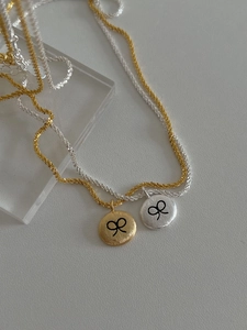 Detail of gold and silver brushed round pendants with black bow design on shimmer chains