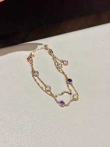 Gros plan d'un bracelet double chaîne dorée avec des pierres de zircon colorées