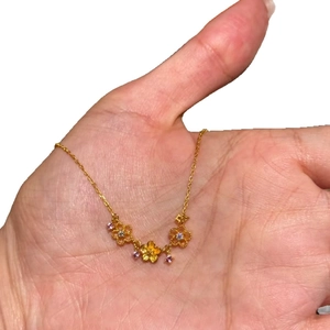 Collier floral doré avec zircons violets tenu en main sur un fond blanc épuré