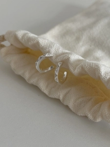 Macro shot of silver geometric hoop earrings with diamonds on a linen jewelry pouch