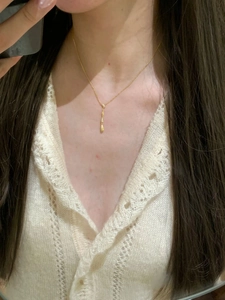 Dettaglio di una collana con pendente a goccia d'oro a strati su un maglione color crema