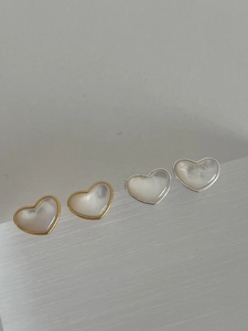 Close-up of gold and silver heart-shaped stud earrings with iridescent pearl inlay