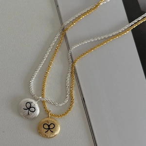 Brushed circular pendant necklace with bow engraving in gold and silver finish