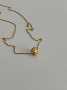 Close-up of golden cylinder pendant with floral relief and small white crystal