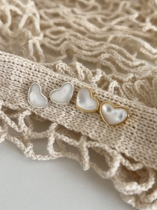 Close-up of heart-shaped earrings in gold and silver finish with white shell inlay