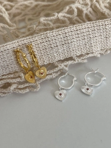 Dettaglio di orecchini a cuore S925 oro e argento con pietre rosse su pizzo fine